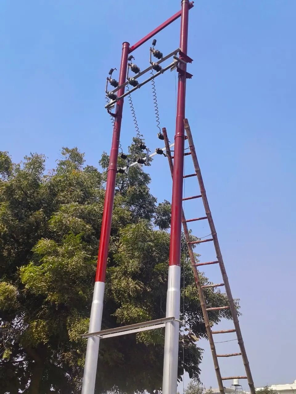 Double-pole structure with insulators and a ladder, against a clear sky